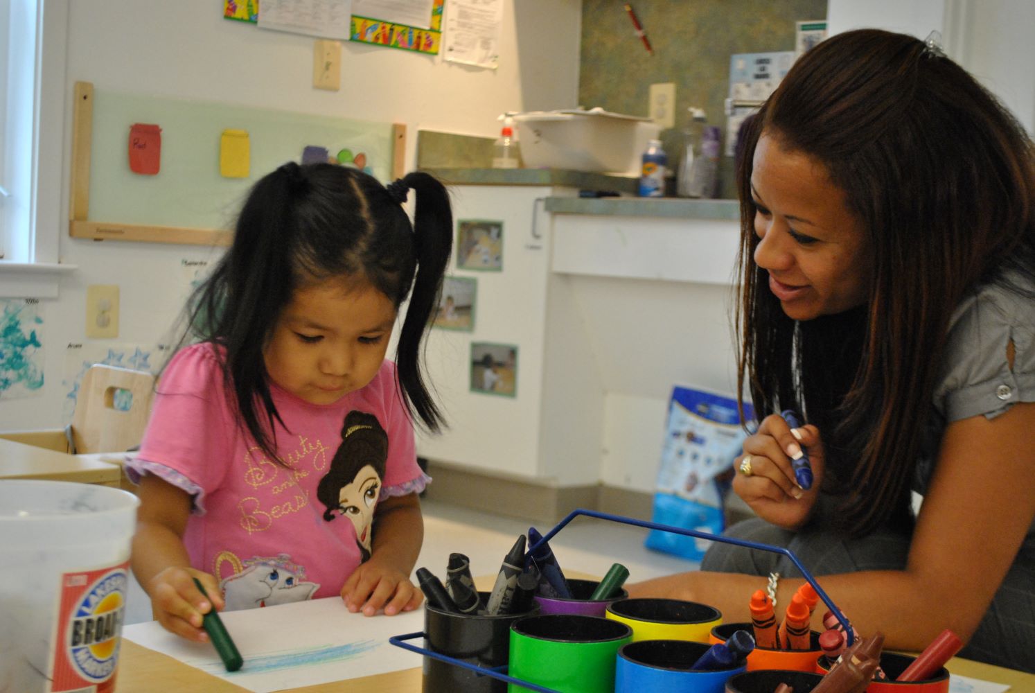 Teacher helping child color with crayons.