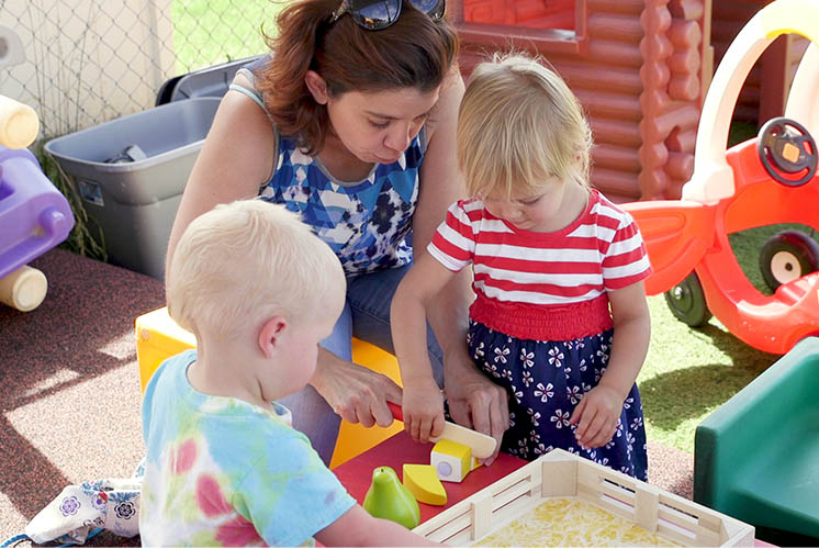 a teacher helps two youngsters cut some playdough