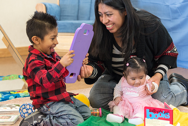 A teacher plays on the floor with a boy and a baby