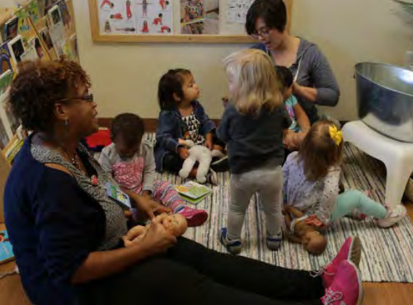 Maestras sentadas en el suelo con niños pequeños