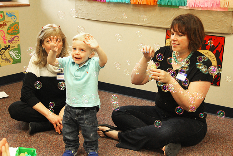 Teachers play with a toddler using bubbles