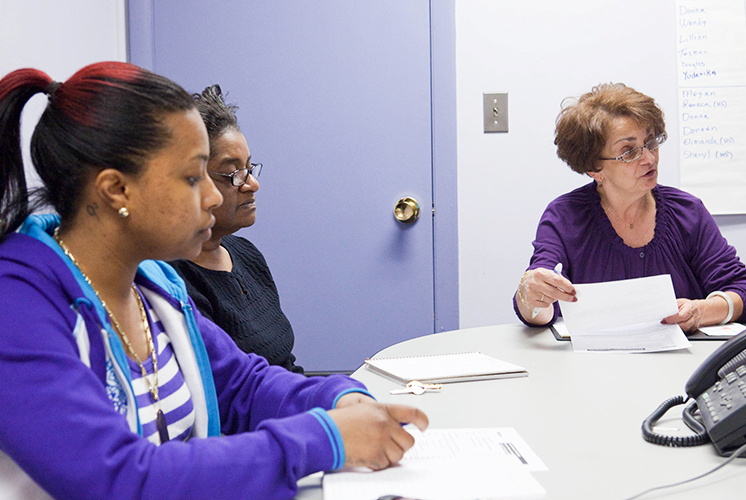 three women sit at an office table and consult notes