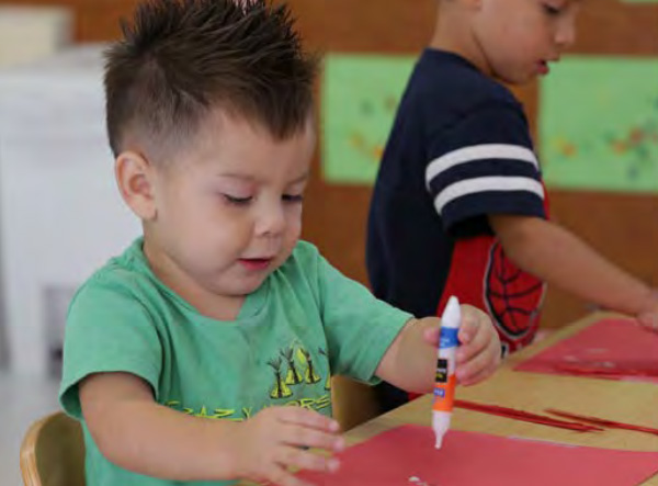 Toddler boy creating art with glue and red construction paper