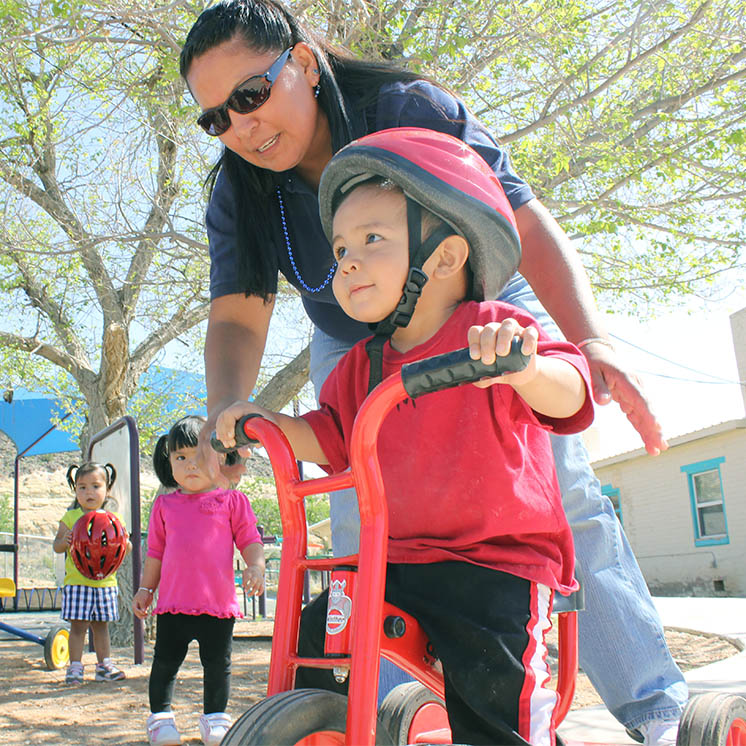 a teacher helps a boy in a bike helmet navigate on a tricycle