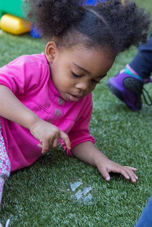 a girl lying on turf examines some bubbles