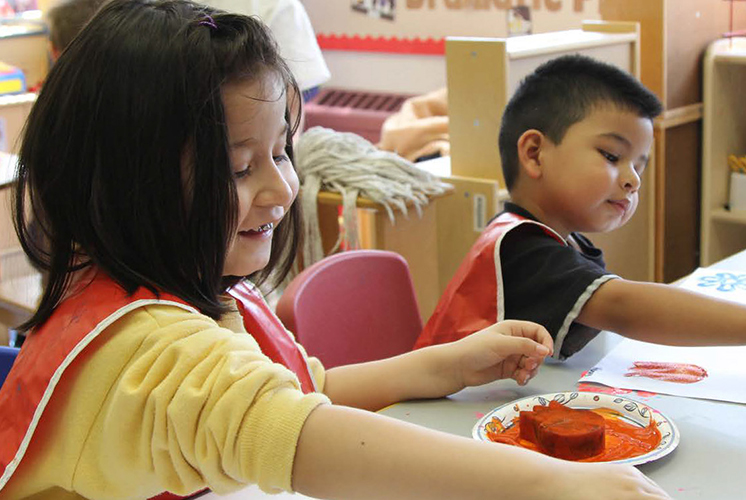 Un niño y una niña juegan con pintura y esponjas en una mesa