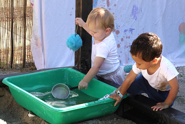 unos niños juegan con agua en una bañera que se encuentra en la parte superior de una caja de arena