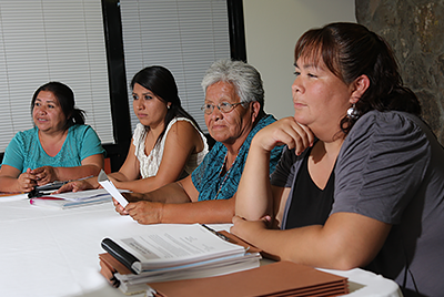 Cuatro mujeres sentadas en una mesa de oficina escuchando a alguien fuera de la cámara