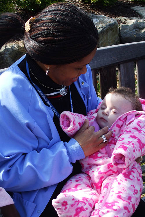 A woman sits outdoors on a bench and cuddles a baby