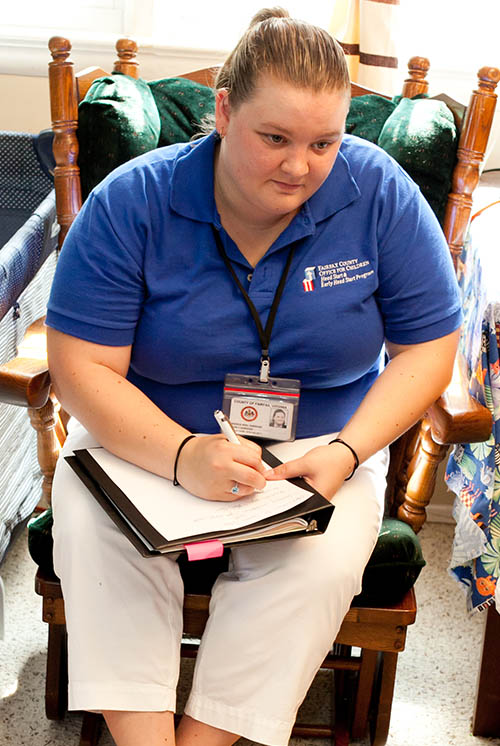 a teacher sitting in a chair in the playroom is taking notes