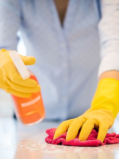 Persona que usa guantes, rocía y limpia la superficie.